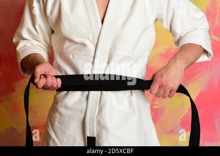 Karate fighter with fit strong hands gets ready to fight. Male body and sportive arms on colorful background. Guy poses in white kimono with black belt. Defence and taekwondo sports concept Stock Photo