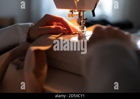 Anonymous woman sewing garment under illumination on machine in dark home studio Stock Photo
