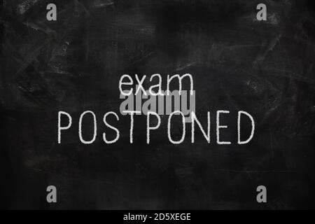 Exam postponed written with white and red chalk on blackboard in classroom Stock Photo