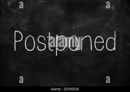 Postponed written with white and red chalk on blackboard in classroom Stock Photo