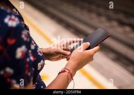 Hand woman waiting on subway platform with her cell phone. Blurred railway on the background. Stock Photo