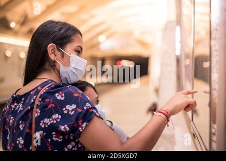 Young mother pointing and showing her daughter on the map where they are going to go. Concept of transport in the new normal with medical masks. Stock Photo