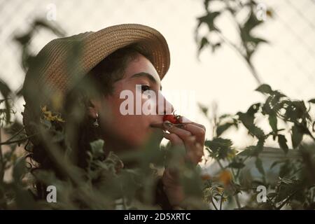 Close-up of a girl smelling a cherry tomato in the garden. Orchard concept Stock Photo