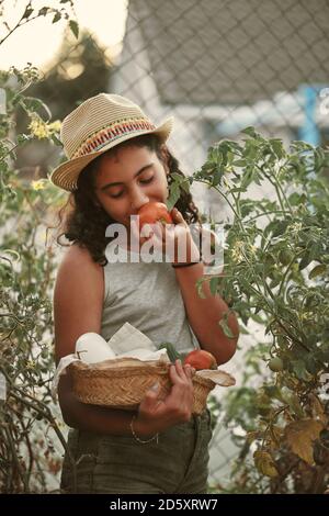portrait of a girl smelling a tomato in her small garden. Orchard concept Stock Photo