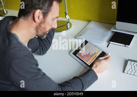 Businessman analyzing bar chart on tablet in office Stock Photo