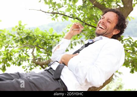 Germany, relaxed businessman lying in tree smoking a joint Stock Photo