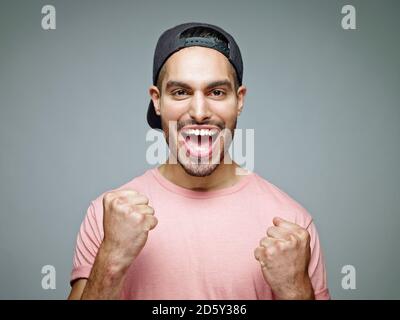Portrait of man with baseball cap screaming for joy in front of grey background Stock Photo