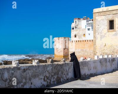 Morocco, Essaouira, Berber in black djellaba at harbor wall Stock Photo