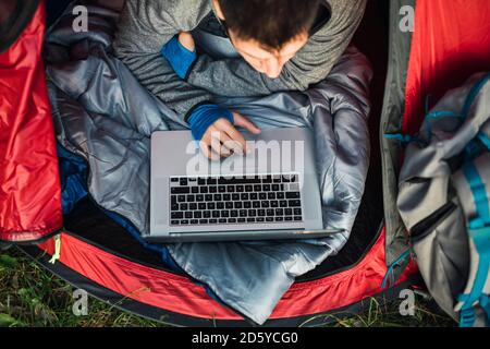 Man camping in Estonia, sitting in tent, using laptop Stock Photo