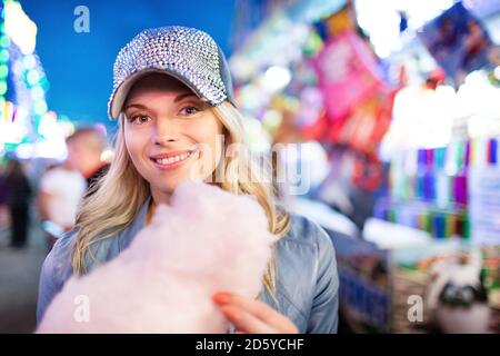 Young woman at fun fair eating candy floss Stock Photo