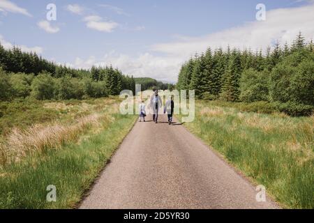 Back view of father hiking with his sons on country road, Cairngorms, Scotland, UK Stock Photo