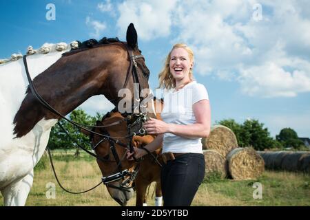 Germany, Wiesenau, laughing blond woman with two horses on a meadow Stock Photo