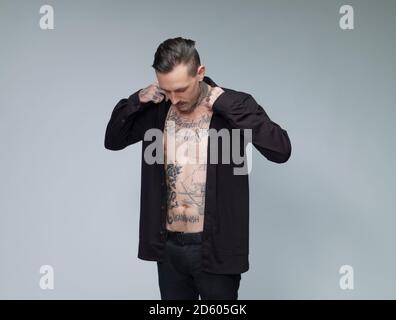 Man with tattoo on his waist up dressing black shirt in front of grey background Stock Photo