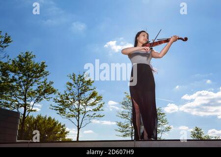 Young female Asian playing violin in front of sky Stock Photo