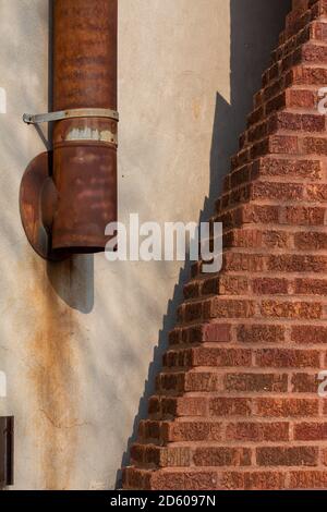 Large rusty exhaust pipe on the side of a vintage white stucco and red brick wall texture background with brickwork in an ornamental pyramid design Stock Photo