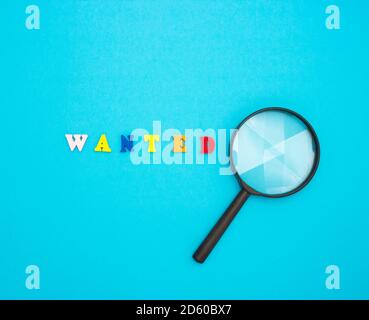 Search for employees to work. The word WANTED in colored wooden letters on a blue background and a magnifying glass. Stock Photo