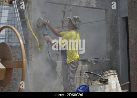Worker or bricklayer, cutting wall with machine by hand, without protection, with buckets, aluminum ladder and ceramic tiles in the background Stock Photo