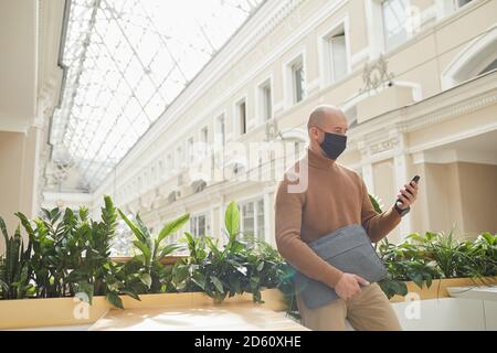 Mature man in protective mask using his mobile phone while waiting for somebody in cafe Stock Photo