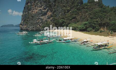 Philippines ocean bay aerial: passenger ships at sandy coast. Local cruise tour for tourists, travelers on boats at sea gulf of El Nido Islands, Asia. Tropical nature landscape in cinematic drone shot