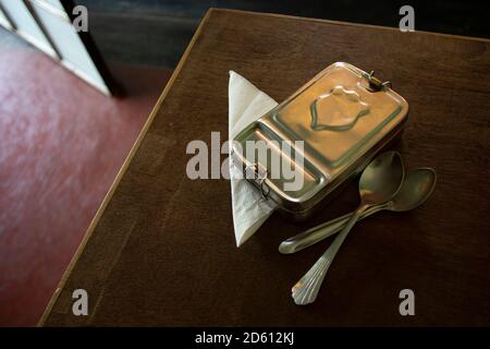 Bolpur, West Bengal/India - 10.10.2020: Vibrant metal lunch box with steel spoons - top view, close up. Paper napkin and household food utensils. Stock Photo