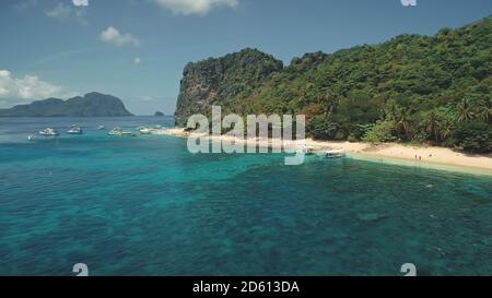 Ocean bay harbour with boats and passengers at sand beach aerial view. Panoramic landscape of tropic island with tourist. Green forest at shore with travelers at vessels on Palawan Isle, Philippines Stock Photo