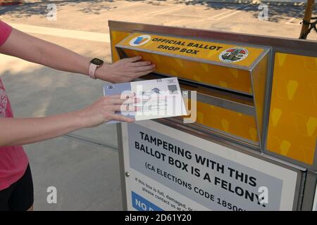 Los Angeles, CA / USA - Oct. 14, 2020: A woman puts a ballot for the 2020 presidential election in an official ballot drop box in L.A. County. Stock Photo