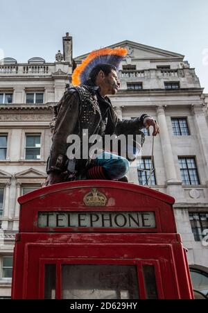 Punk rocker with mohican hair sits relaxing on top of red telephone boxes in central London, England, United Kingdom Stock Photo