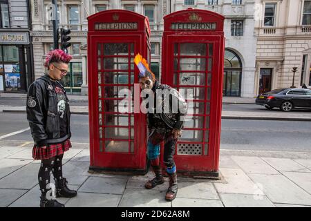 Punk rocker with mohican hair sits relaxing on top of red telephone boxes in central London, England, United Kingdom Stock Photo