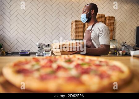 Afro American man in medical mask holding pizza boxes Stock Photo