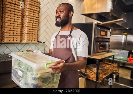 Cheerful male worker holding container with leafy greens Stock Photo
