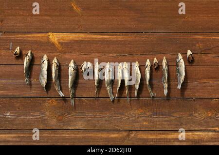 A bunch of dried salted fish hangs on a background of wooden planks Stock Photo