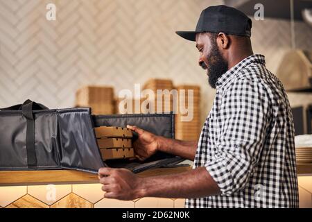Handsome Afro American man putting pizza boxes in delivery bag Stock Photo