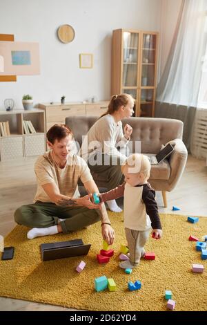 Mother and father using their computers they working at home with their child playing with toys Stock Photo