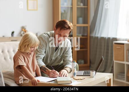 Father sitting at the table with his son and teaching him they are in the living room at home Stock Photo