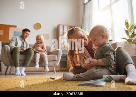 Happy mother playing with her baby on the floor and father playing with older son in the background in the room Stock Photo