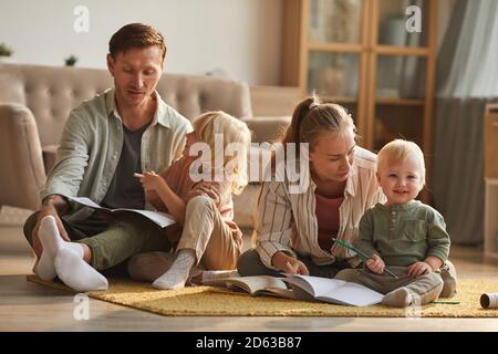 Two parents sitting on the floor and reading a book to their small sons in the living room at home Stock Photo