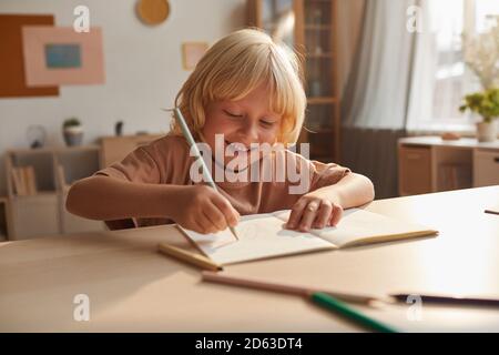 Little boy sitting at the table and making notes in notebook he doing his homework at home Stock Photo