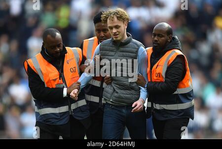 A pitch invader is assorted off the pitch by stewards  Stock Photo