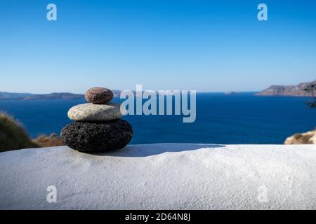 Close-up shot of pebbles stacked on each other in a balance with santorini caldera in the background Stock Photo