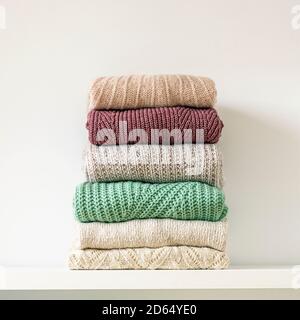 Stack of warm cozy knitted women's sweaters on white background. Autumn or winter comfort concept. Stock Photo