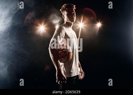 Football. Mulatto guy standing isolated on dark filed posing with ball sassy side view Stock Photo