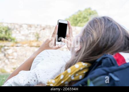 a Mockup image of unrecognizable young womans hands holding white mobile phone with blank black screen held up in hands while lying and chilling in th Stock Photo