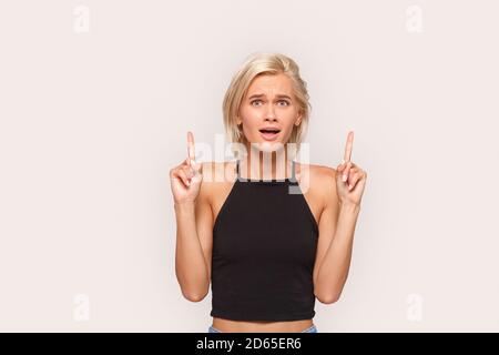 Freestyle. Young blonde woman in top standing isolated on white pointing up at copy space smiling excited Stock Photo