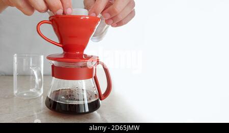 Man brews at home v 60. He puts paper filter in ceramic dripper and pours hot water, preparing filter for pouring coffee Stock Photo