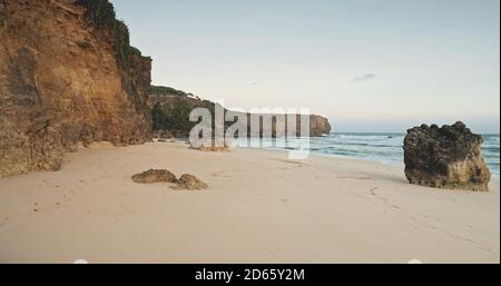 Sand rock coast waves of ocean bay aerial view. Nobody nature landscape of cliff shore with stones at sandy sea shoreline. Summer tropic Indonesia mesmerizing seascape at soft light cinematic shot Stock Photo