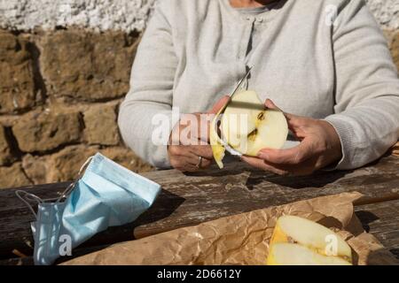 A senior woman, peel half an apple to eat at the mountain hut of the fountain of Artica, in Luesia, Spain. Stock Photo