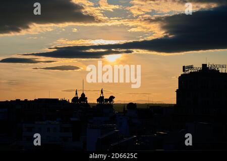 Sun breaking through dark clouds over silhouetted rooftops and quadrigas on Calle de Alcalá, Madrid at sunset Stock Photo