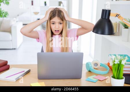 Oh no i fail my semester test. Frustrated kid girl sit table desk study remote use laptop upset about her exam results touch hands head in house Stock Photo