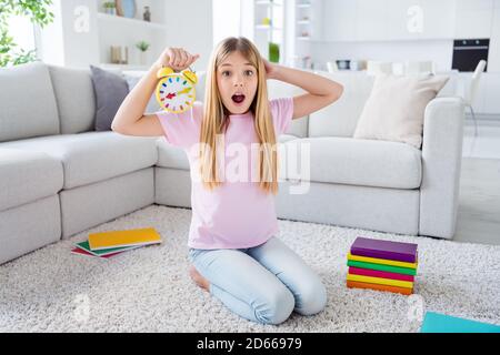 Oh no i miss online lesson. Full size photo of amazed frustrated kid girl sit floor carpet hold clock touch hand head scream omg in house indoors Stock Photo