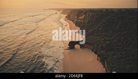 Sunset ocean seascape with waves at rock wall on sand beach aerial view. Nobody nature scenery at summer evening with amazing seascape at cliff sea shore. Soft light Indonesia sun set scape Stock Photo